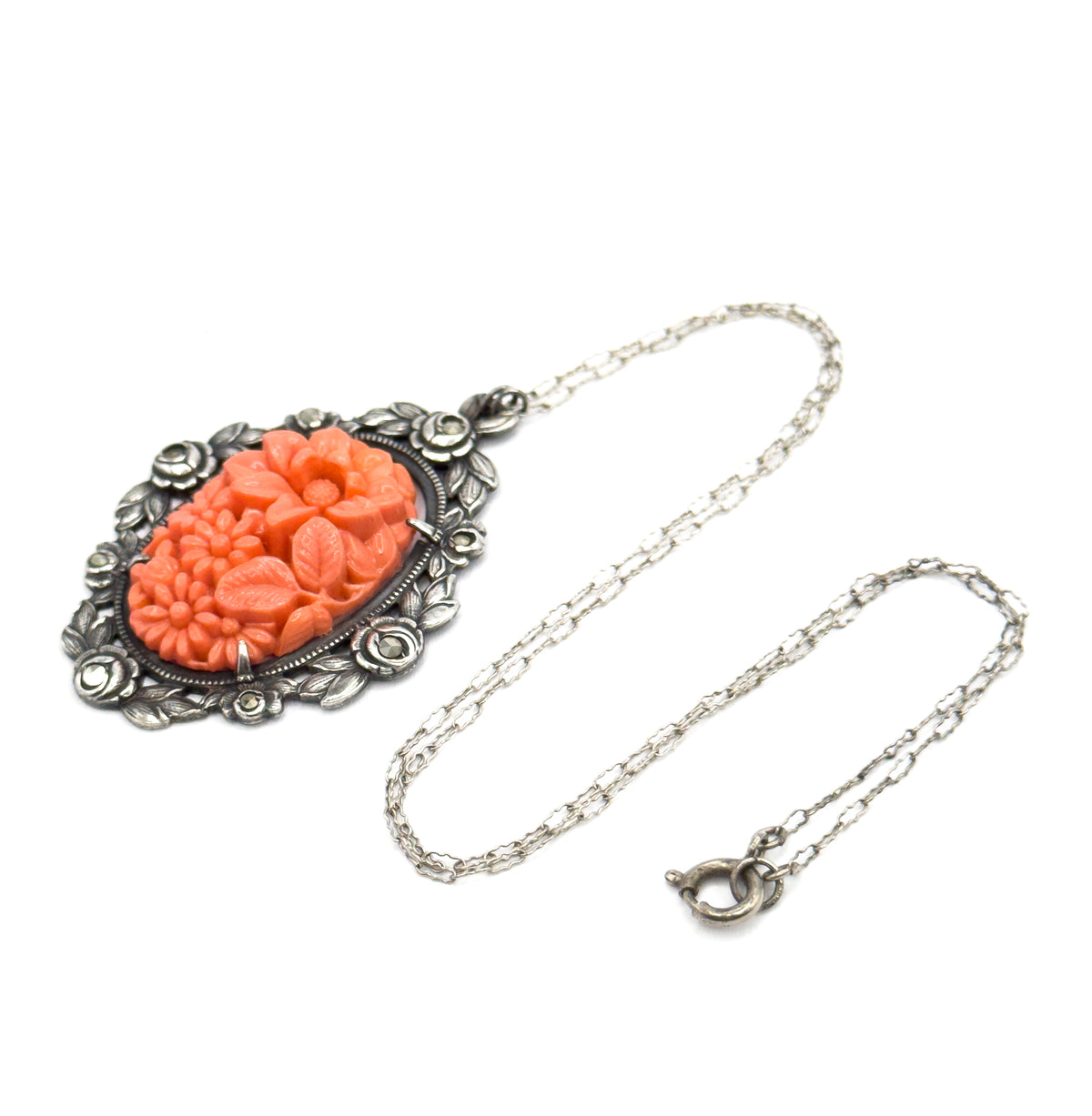 Laid flat with the chain looped out to one side and the spring ring clasp at the far end, the pendant angled at upper left so its patinated silver frame and coral-coloured glass centre face up.