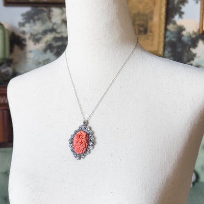 Art Deco coral glass and marcasite pendant in sterling silver, shown at the neck of a pale linen bust form, its oval leaf-edged frame hanging from a fine chain.