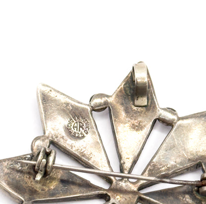 Close-up of the upper reverse, where the AR maker's stamp in a circle sits on one silver point beside the folded bail and the pin stem crossing beneath.