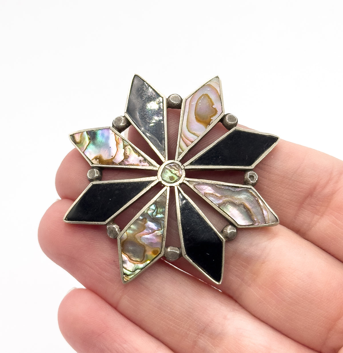 Shown resting across four fingers, which gives its scale — the starburst spans about the width of three fingertips — with silver ball accents between each onyx and abalone point.