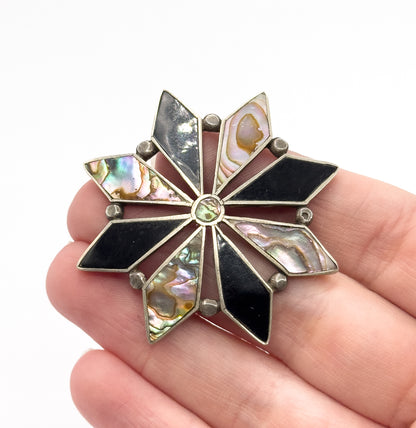 Shown resting across four fingers, which gives its scale — the starburst spans about the width of three fingertips — with silver ball accents between each onyx and abalone point.