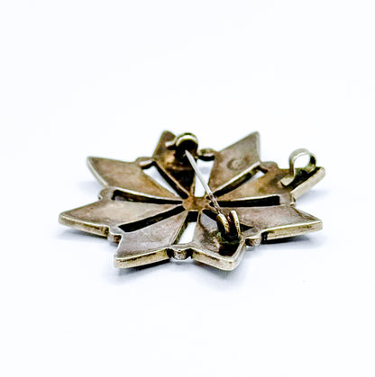 Low, tilted view of the reverse with the brooch angled away, showing the open pin stem lifted above the back, the catch and joint, and the small bail standing out at the right edge.