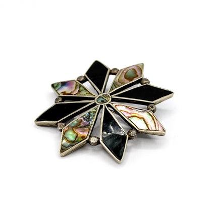 Low, near-level view of the face, so the silver bezel walls around each onyx and abalone point show their depth and the centre stone sits almost edge-on.