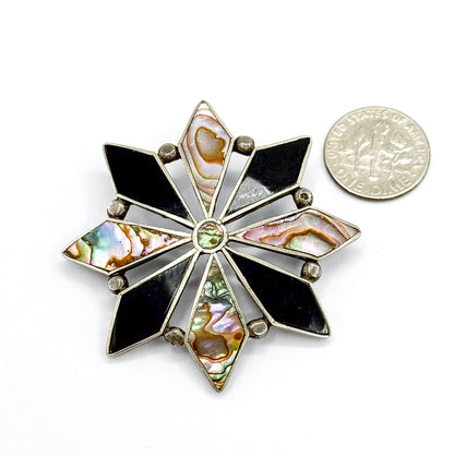 The starburst face flat on white beside a dime, which shows its size — the brooch is roughly two and a half times the coin's width across the onyx and abalone points.