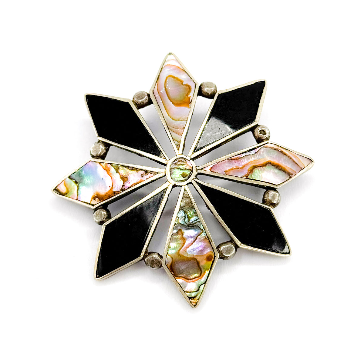 Straight-on overhead view of the whole face on white, the eight onyx and abalone points evenly spaced around the small round centre bezel so the full starburst symmetry reads clearly.
