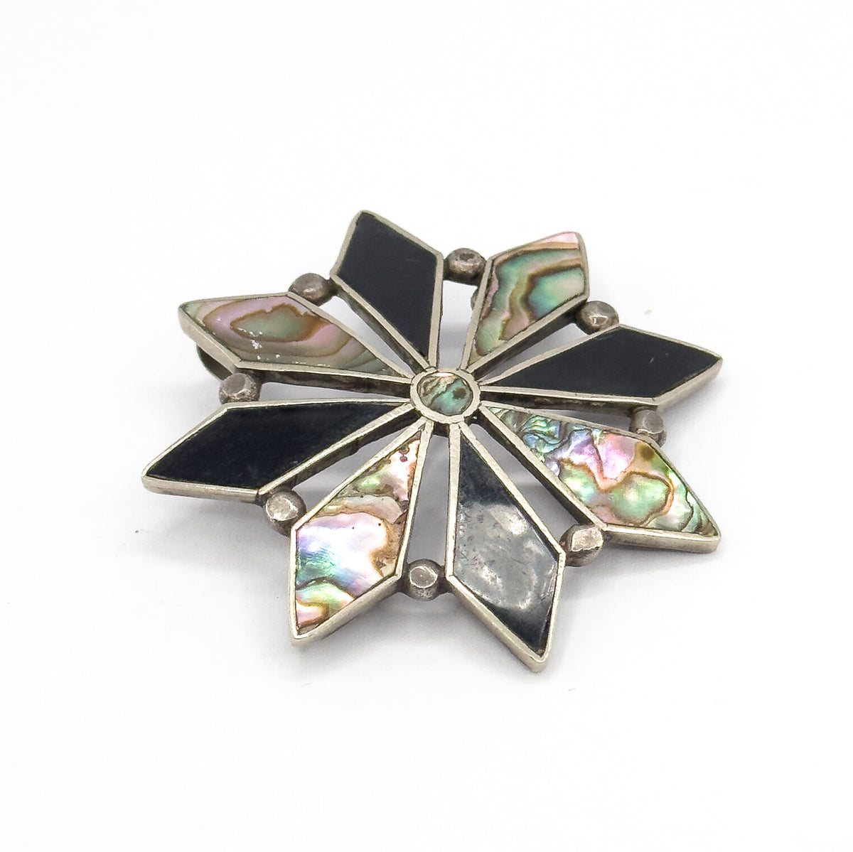 Vintage starburst brooch in sterling silver, shown face-up at a slight angle on white, its eight diamond-shaped onyx and iridescent abalone inlays radiating from a small centre bezel.