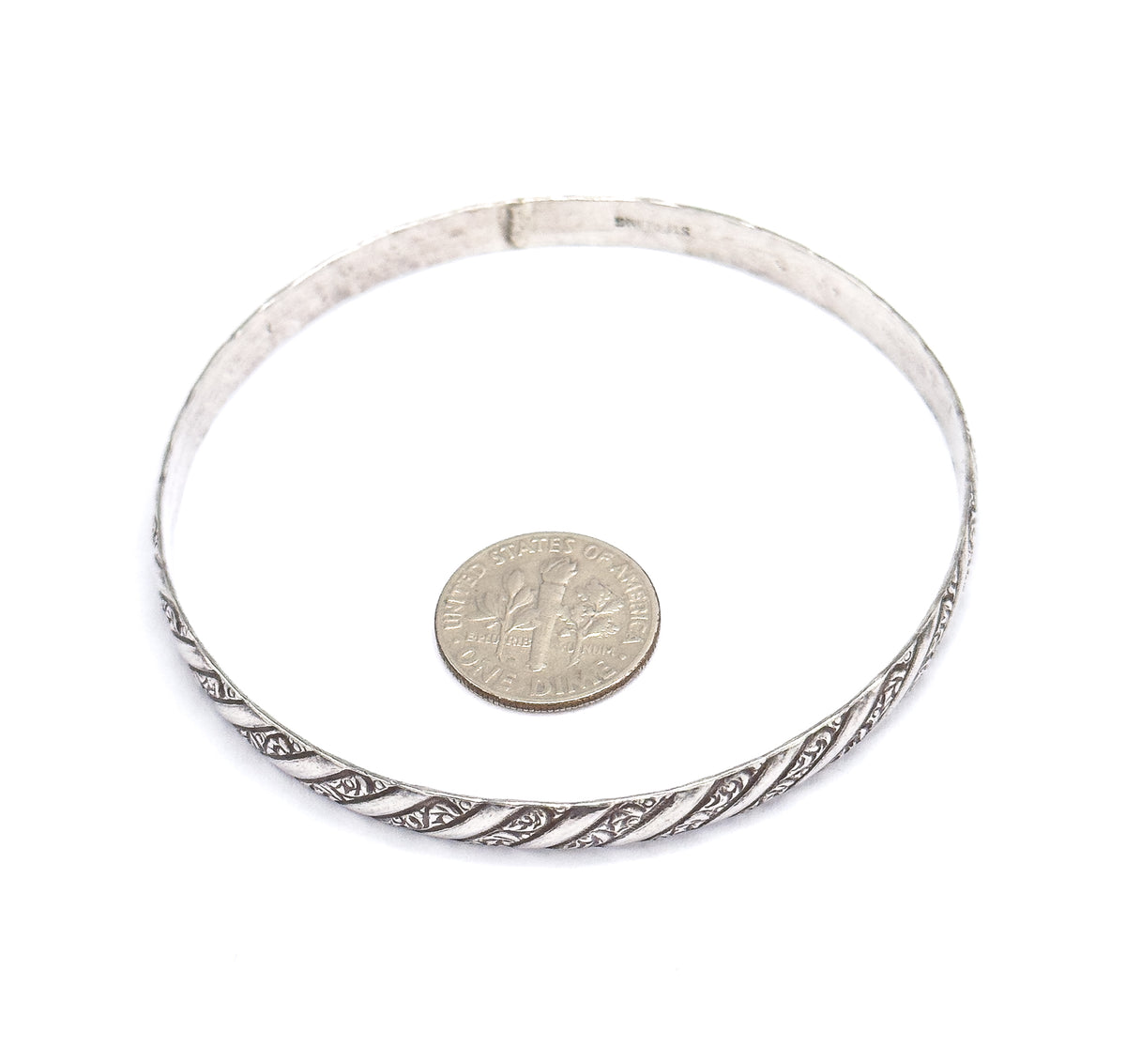 Laid flat on white with a dime inside the circle for scale, showing the full round of the sterling silver bangle and its repousse spiral pattern across the front edge.
