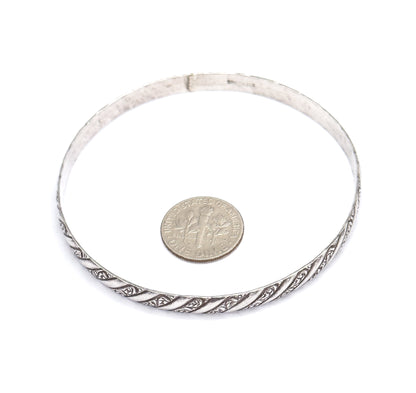 Laid flat on white with a dime inside the circle for scale, showing the full round of the sterling silver bangle and its repousse spiral pattern across the front edge.