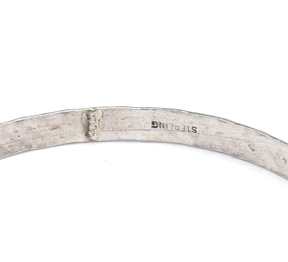 Close view of the smooth inner surface of the bangle, where the metal is stamped with a maker's mark and the word sterling.