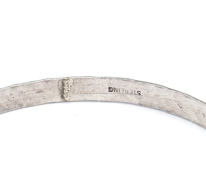 Close view of the smooth inner surface of the bangle, where the metal is stamped with a maker's mark and the word sterling.