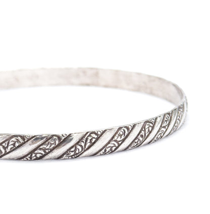 Macro of the outer band at an angle, where the diagonal repousse stripes of scrolling leaf detail alternate with plain raised ribs, darker patina settled in the recesses.