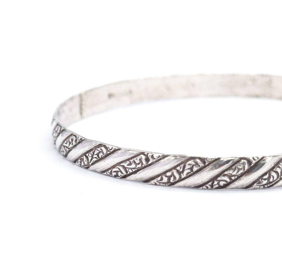 Three-quarter view of the bangle standing on edge and curving away from the camera, the repousse spiral stripes sharp along the near rim while the plain inner wall recedes behind.