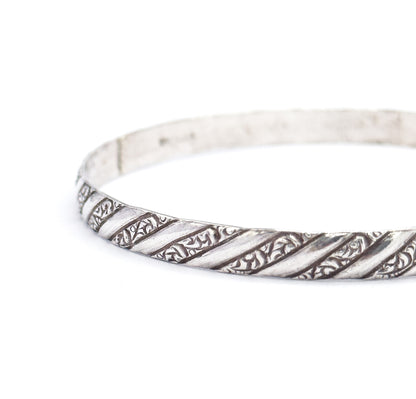 Three-quarter view of the bangle standing on edge and curving away from the camera, the repousse spiral stripes sharp along the near rim while the plain inner wall recedes behind.