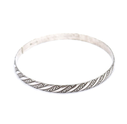 The whole bangle tilted almost flat to the camera so the full circle and its open centre are visible, repousse stripes running along the near rim and the plain band fading at the back.