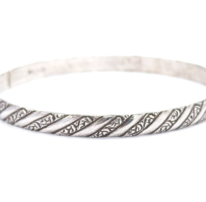 Close view of the lower front arc of the sterling silver bangle, the diagonal repousse stripes crisp across the foreground while the plain upper band sweeps out of focus behind.