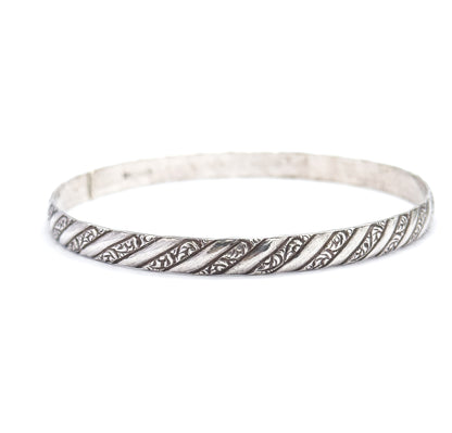 The bangle lies tilted low and nearly edge-on, its smooth inner wall and faint stamped mark visible at the back while the repousse stripes run unbroken along the front rim.