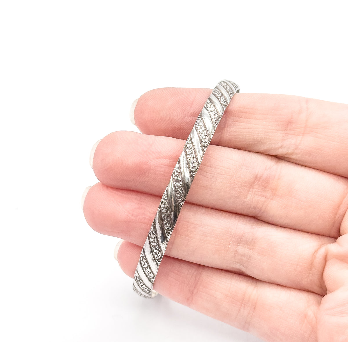 A sterling silver repousse bangle held across the fingers of a hand, its spiralling textured band visible edge-on, giving a sense of its narrow width and scale.