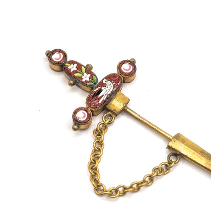 Close view of the mosaic hilt, its cross-shaped panels showing a white dove, white flowers and crescents on rust ground, with the chain swagging below the stem.