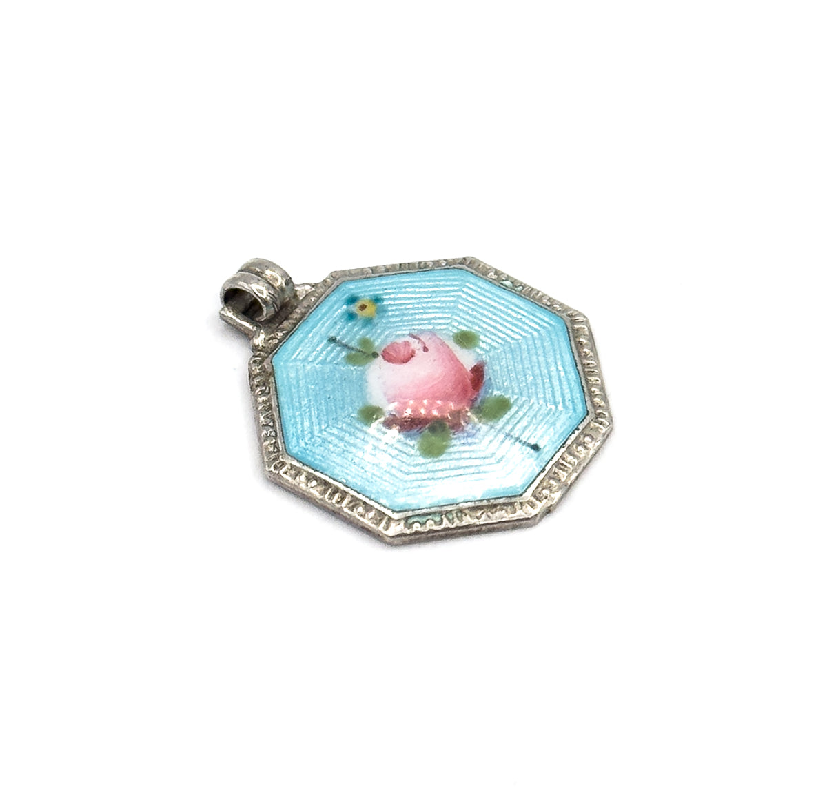 The charm turned so the ribbed bail sits at the upper left, the full octagon of the frame visible with its eight short facets framing the blue enamel field and its central pink rose.