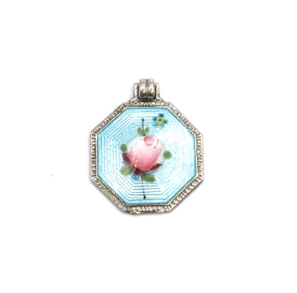 The octagonal enamelled face shown squarely head-on with the ribbed bail upright at the top, the pink rose centred on the pale blue field within its beaded silver frame.