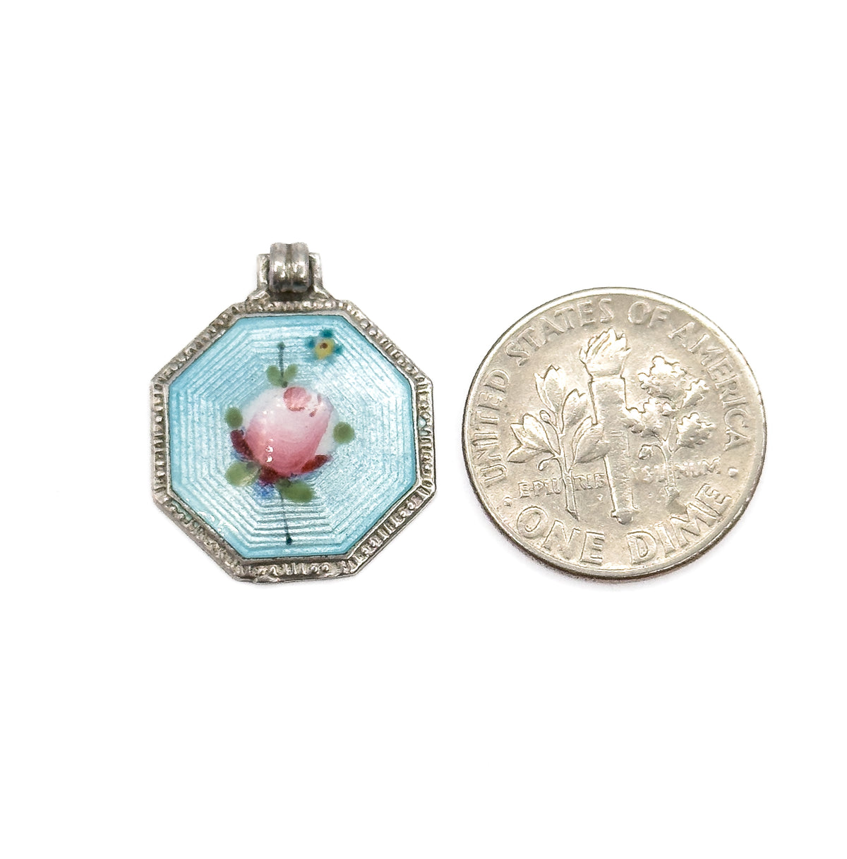 The charm laid beside a dime for scale, its octagonal enamelled face and ribbed bail together standing a little taller than the coin is wide.