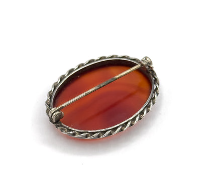 The reverse at an angle, showing the hinged pin stem stretched across the open back of the stone to its catch, framed by the twisted sterling rope edge.