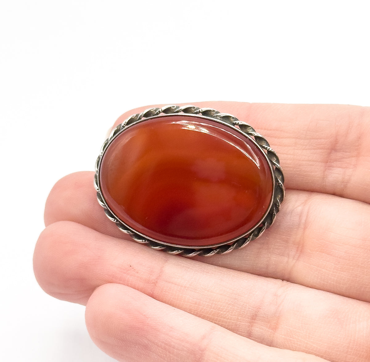 Vintage carnelian agate brooch in sterling silver, the oval banded reddish-brown stone in a twisted-rope sterling bezel, shown resting across fingers to convey its size.