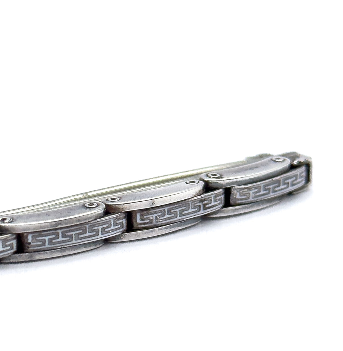 Angled close-up of one end of the bar, where the linked plates show a repeating square-scroll pattern in white against the silver and tiny rivet pins joining each link to the next.