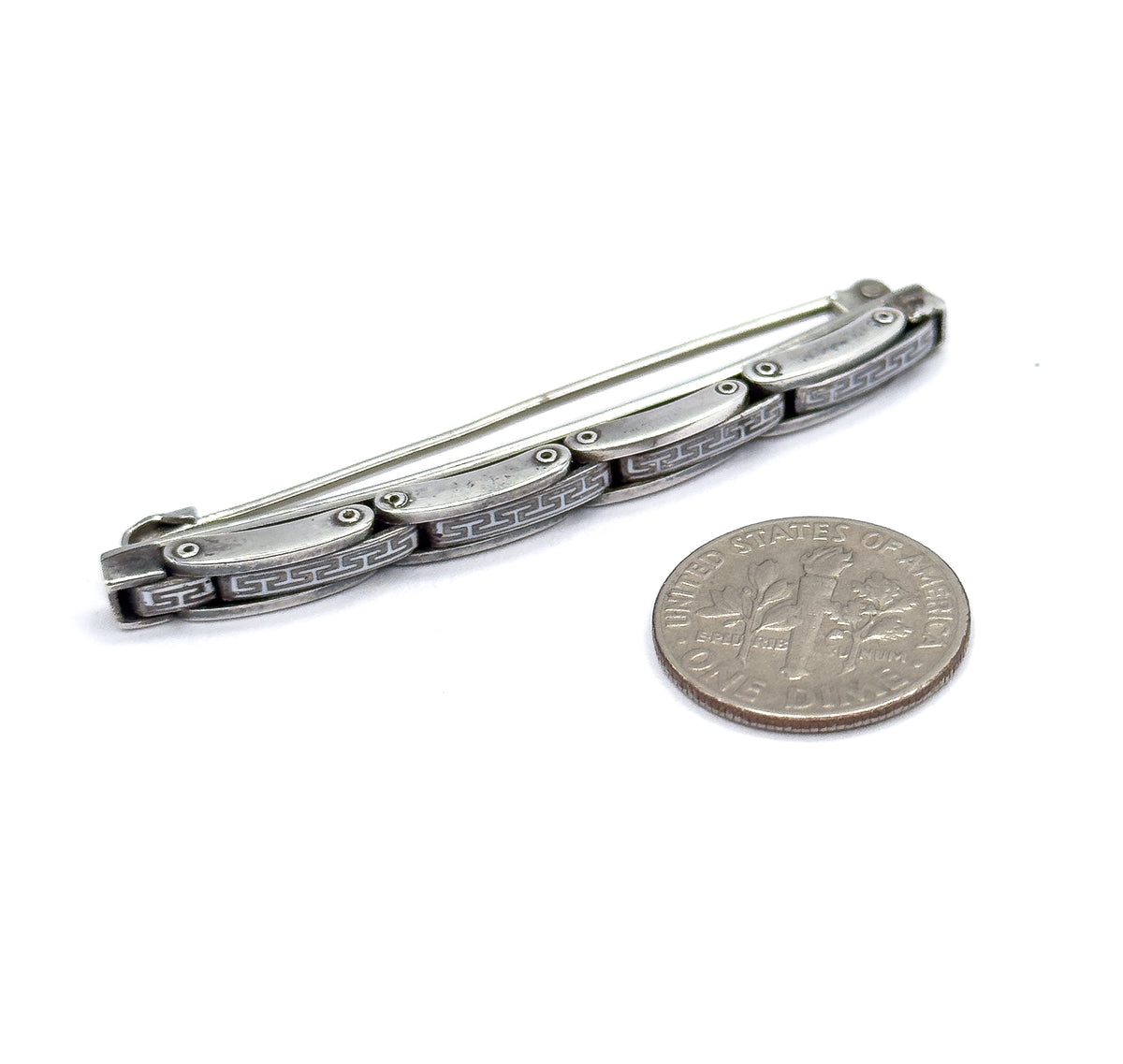 The whole brooch laid beside a dime, the coin showing the slim bar is a little over twice its width, with pin stem and hook catch visible along the back.