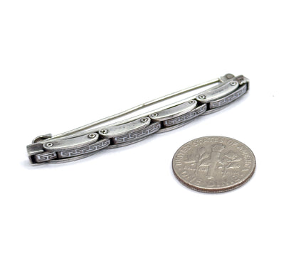 The whole brooch laid beside a dime, the coin showing the slim bar is a little over twice its width, with pin stem and hook catch visible along the back.