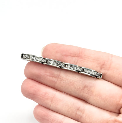 Vintage sterling silver openwork link brooch, a slim bar of geometric links with darkened patina in the recesses, shown resting across the fingers of a hand for scale.