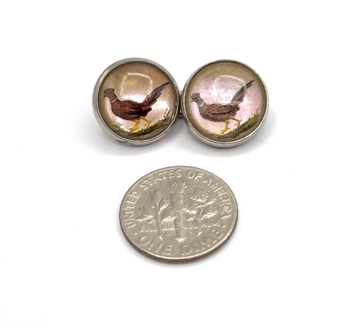 Two round painted faces side by side above a dime, showing the pheasants in their sterling bezels are each well under half the coin's width.