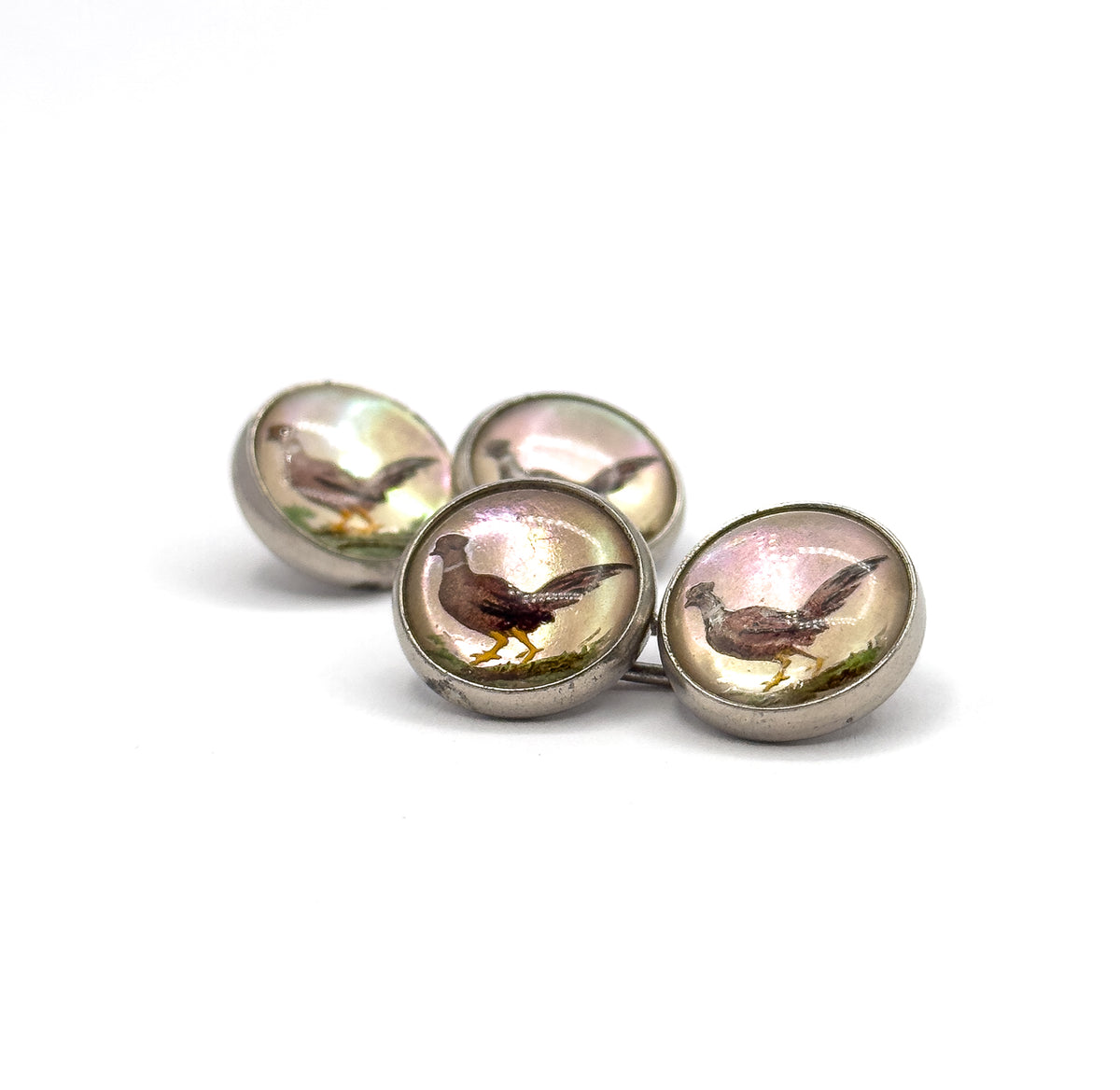 Low three-quarter view at eye level, the four pheasant faces stepping back in a diagonal line so the curved sterling bezel rims and the slender connecting bar between them stand out.