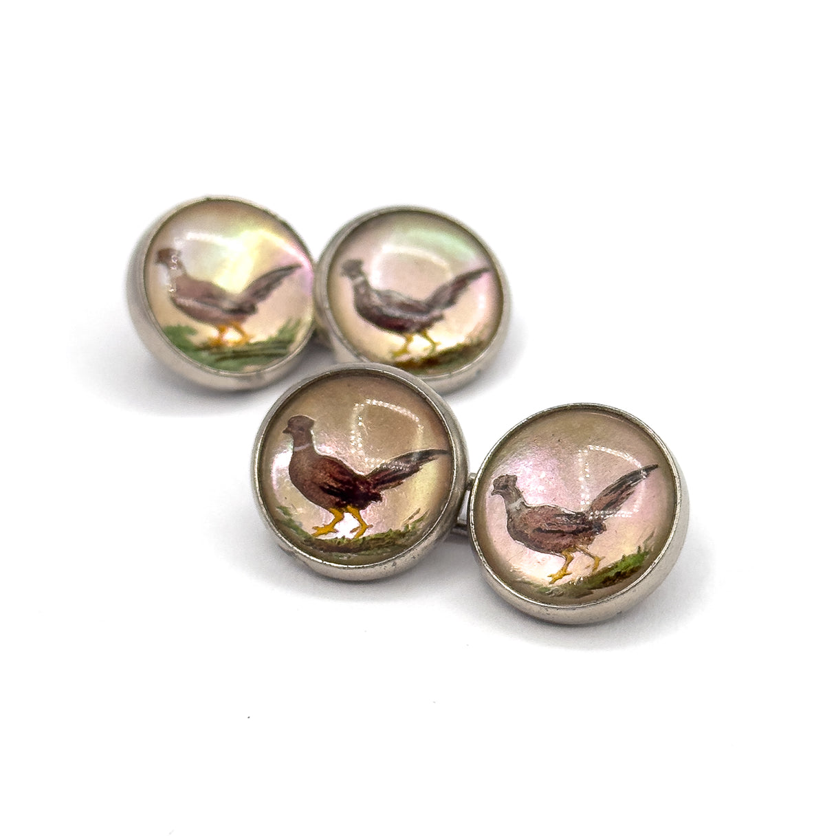 Close overhead angle with the four faces clustered tightly together, filling the frame so each pheasant's brown plumage, yellow legs and green grassy foreground read clearly within its sterling bezel.