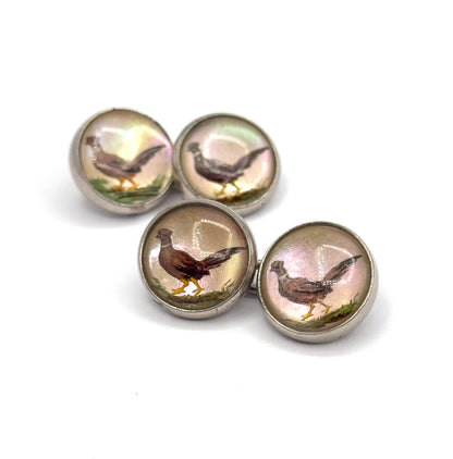 Close overhead angle with the four faces clustered tightly together, filling the frame so each pheasant's brown plumage, yellow legs and green grassy foreground read clearly within its sterling bezel.