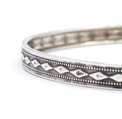Angled view along the band showing the smooth, unpatterned inner surface of the bangle curving away behind the diamond-patterned outer face.