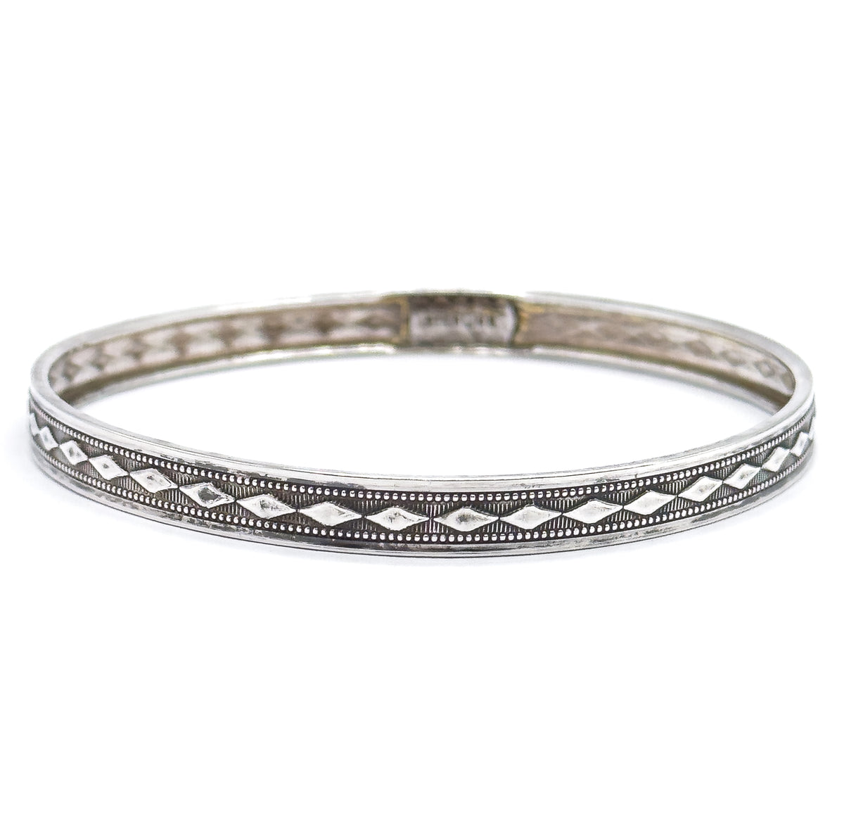 The complete bangle viewed almost edge-on against white, so the diamond band reads as a long unbroken ring across the front with the far inner wall and its small stamped mark visible behind.