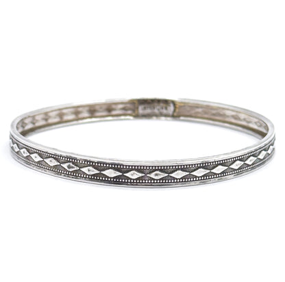 The complete bangle viewed almost edge-on against white, so the diamond band reads as a long unbroken ring across the front with the far inner wall and its small stamped mark visible behind.