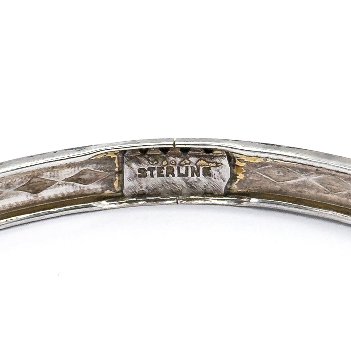 Extreme close-up of the inner surface where the word STERLING is stamped on a smooth rectangular panel, flanked by the faint diamond pattern and darker patina.