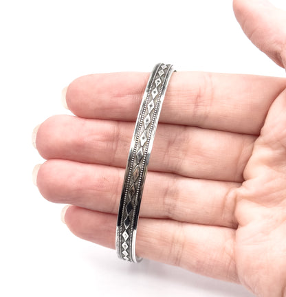 Sterling silver bangle with a repeating diamond pattern along its band, shown resting across the fingers of an open hand, which gives a sense of its size.