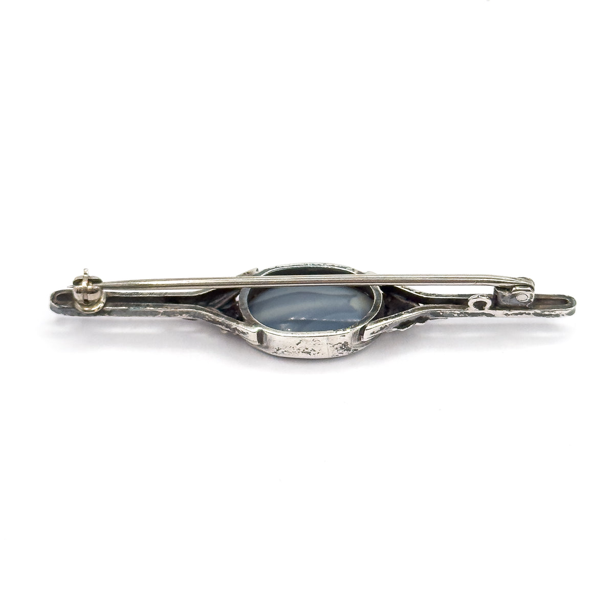 The reverse of the brooch, showing the closed pin stem running the length of the bar, the hinge and catch at each end, and the enclosed back of the oval stone's bezel.