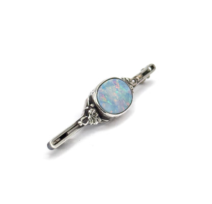 Angled three-quarter view on white, the bar set diagonally so the bezelled opal doublet catches pink and green flashes and the floral silver scrollwork beside it stands out in relief.
