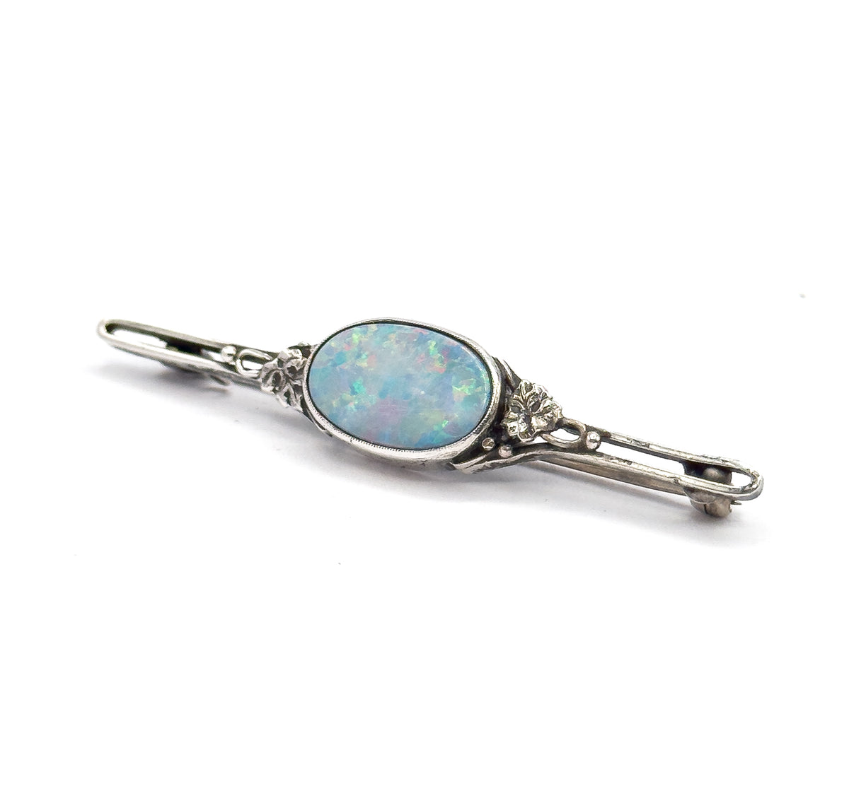 Low, near eye-level diagonal view along the bar, the oval doublet glowing pale blue and green in its bezel while the pin stem and its hooked catch show in profile at the far end.
