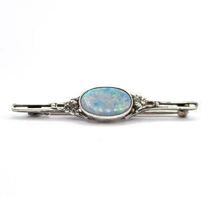 Straight-on front view with the bar level, the oval opal doublet flashing blue, green and pink in its bezel, floral silver mounts at each side and the pin stem just visible behind the bar.