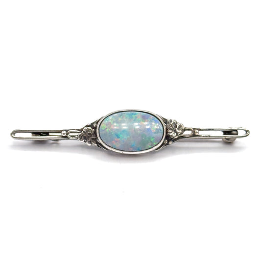 Full-length horizontal view filling the frame, showing the open pierced loops at each end of the bar, the floral silver mounts flanking the bezelled opal doublet, and the catch at the right.
