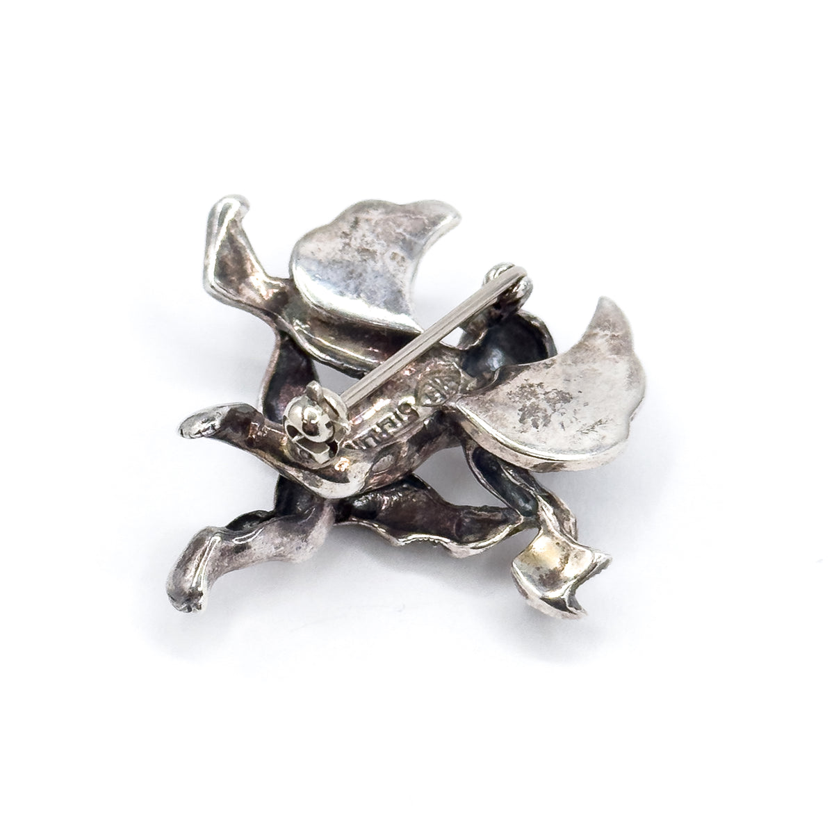 Closer crop of the reverse, tilted so the round safety catch and the pin stem lying across it sit at the centre, with the hollowed backs of the cherub's legs and feet below and patina in the folds.