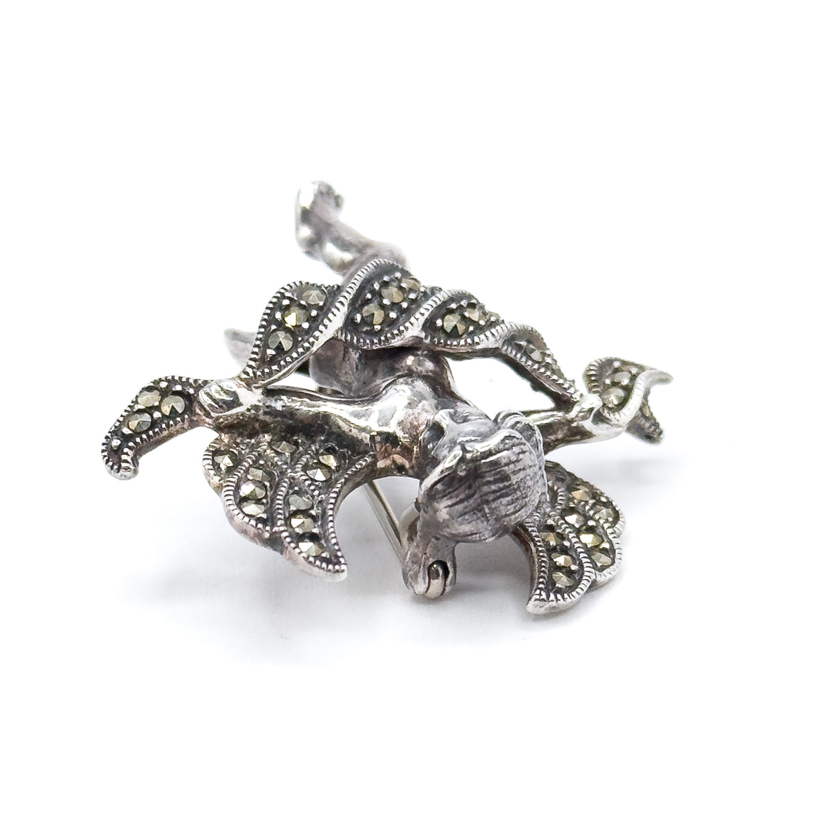 Steep three-quarter view from above the brooch, looking down the sculpted cherub's body and the milgrain-edged wing tips, with the pin stem just showing between the wings behind.