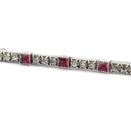 Close-up along the bar's centre, showing three square pink stones in beaded box settings spaced between rows of small clear stones in a light-coloured metal.