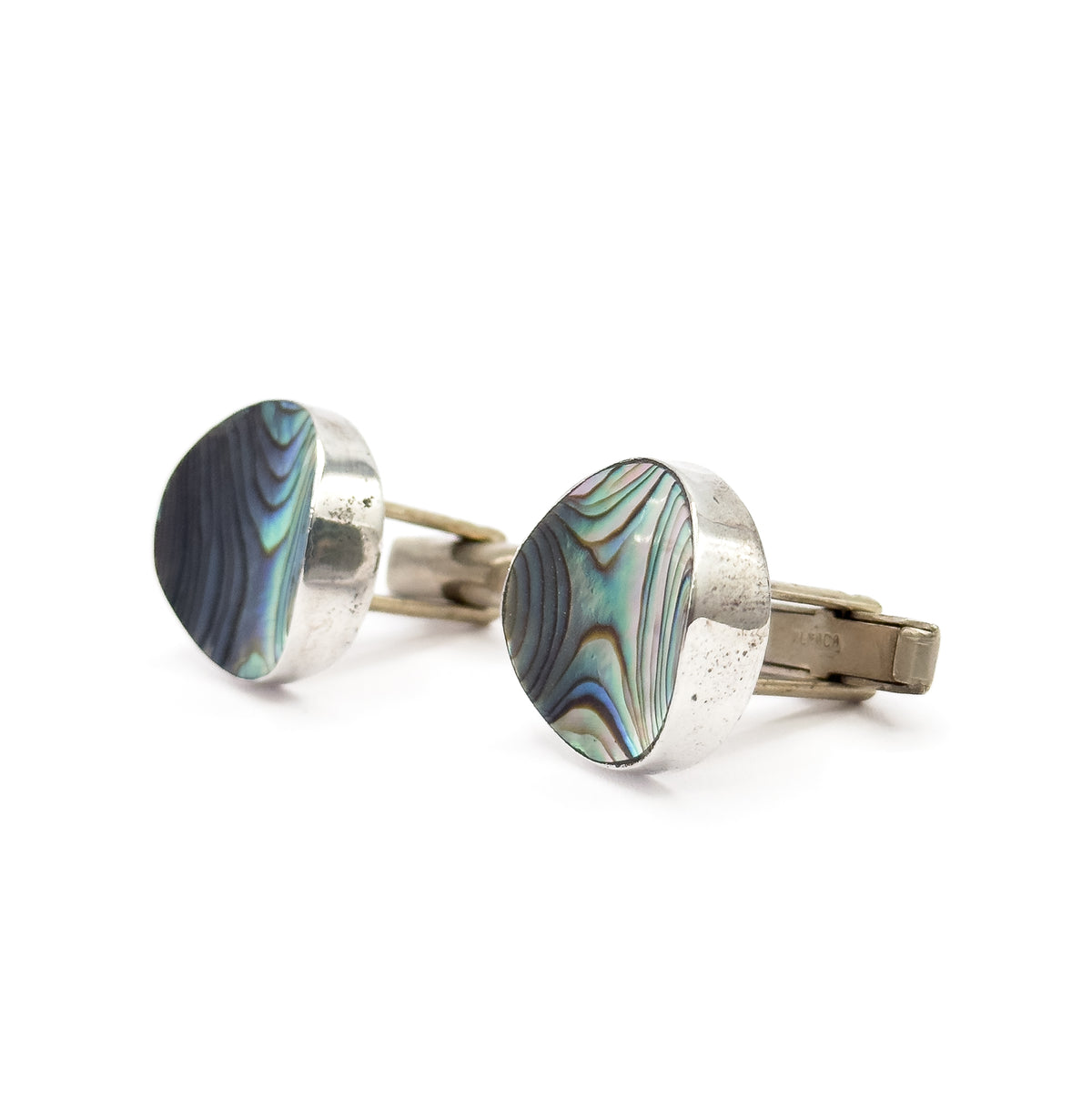 Angled three-quarter view of both faces, the concave abalone shell catching blue and green sheen beside the wide sweep of sterling silver bezel, with both toggle bars trailing to the right.