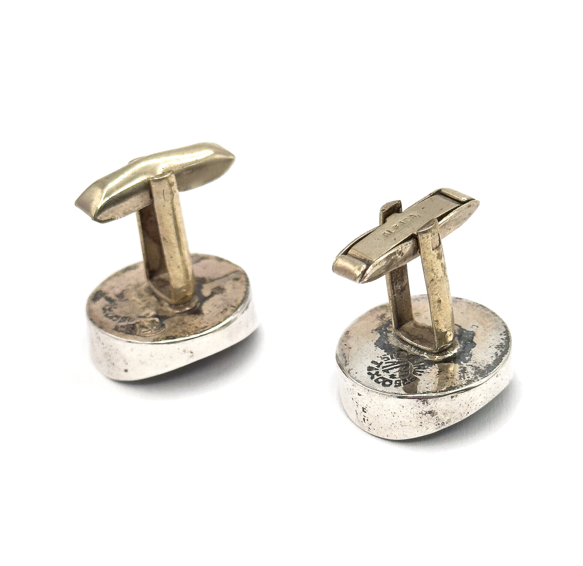 Reverse view of both cufflinks, the rounded sterling silver backs facing up with stamped marks visible and each hinged toggle bar standing upright on its post.